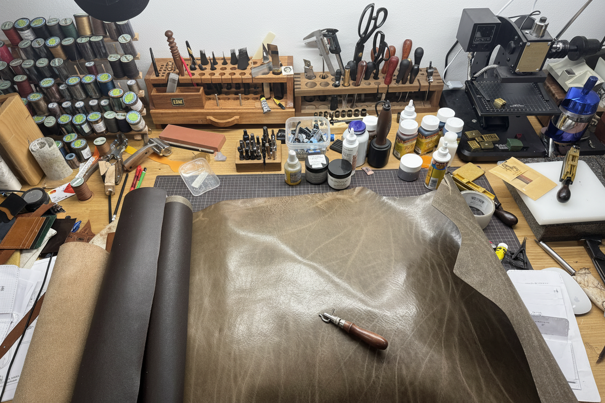 LÅWE workshop bench with a full-grain leather hide laid out for cutting, surrounded by hand tools and thread
