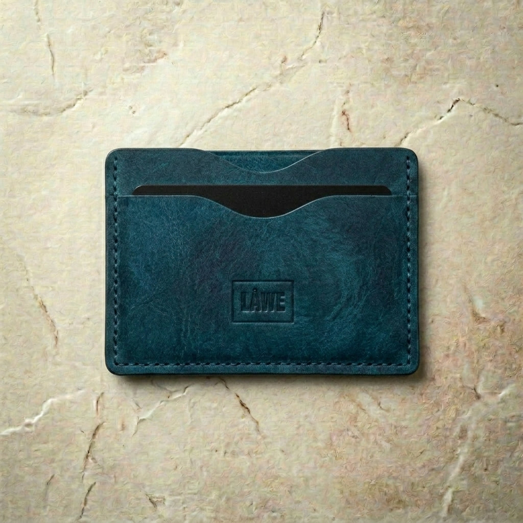 Blue leather cardholder with 'LÅWE' branding on a beige marble background