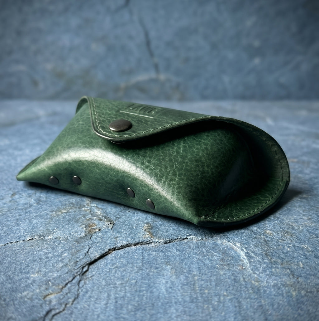 Green leather eyeglasses case with metal studs on a textured blue stone surface