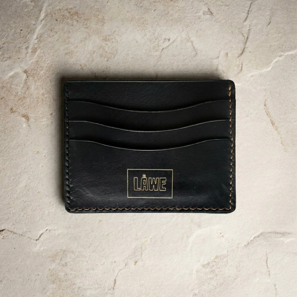 Black leather cardholder with 'LÅWE' branding on a light stone surface
