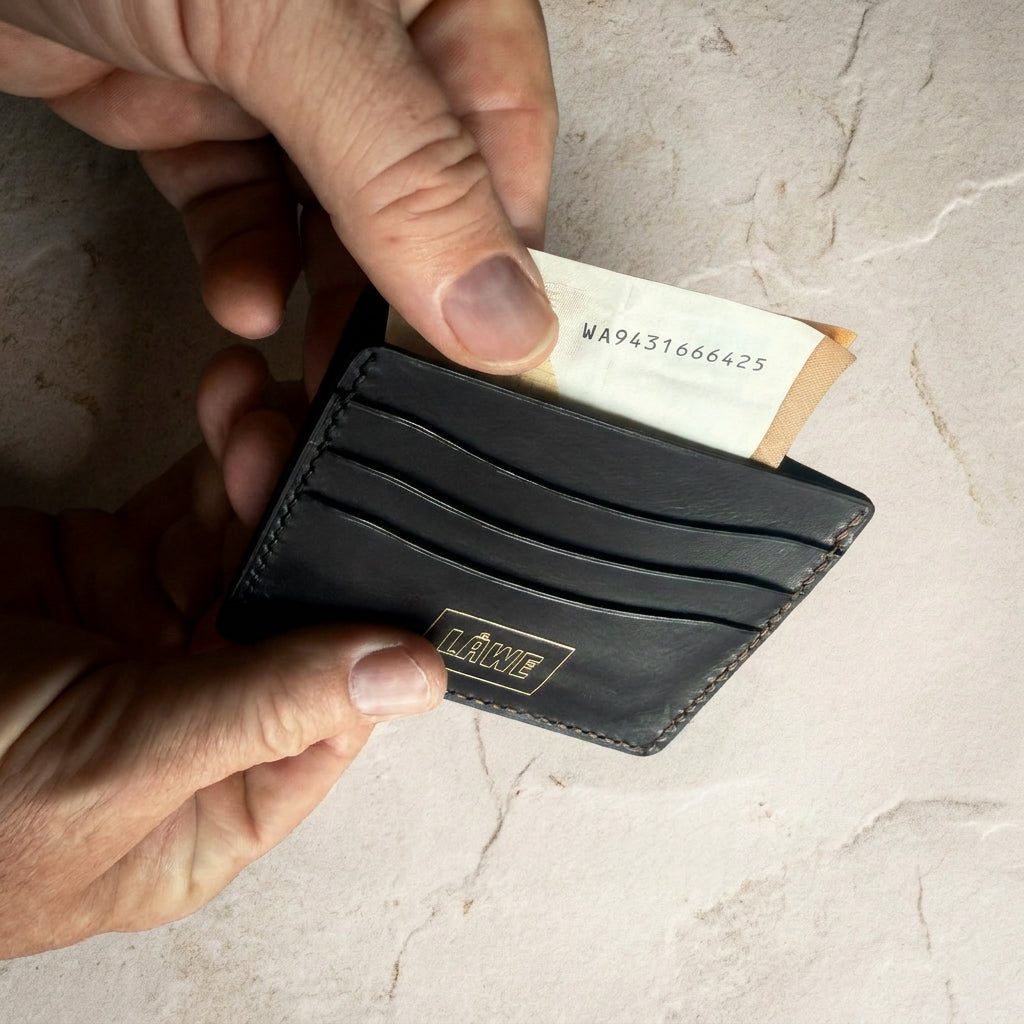 LÅWE Axis Left Handed onyx leather wallet  being used to pull a note out, on a light stone surface.