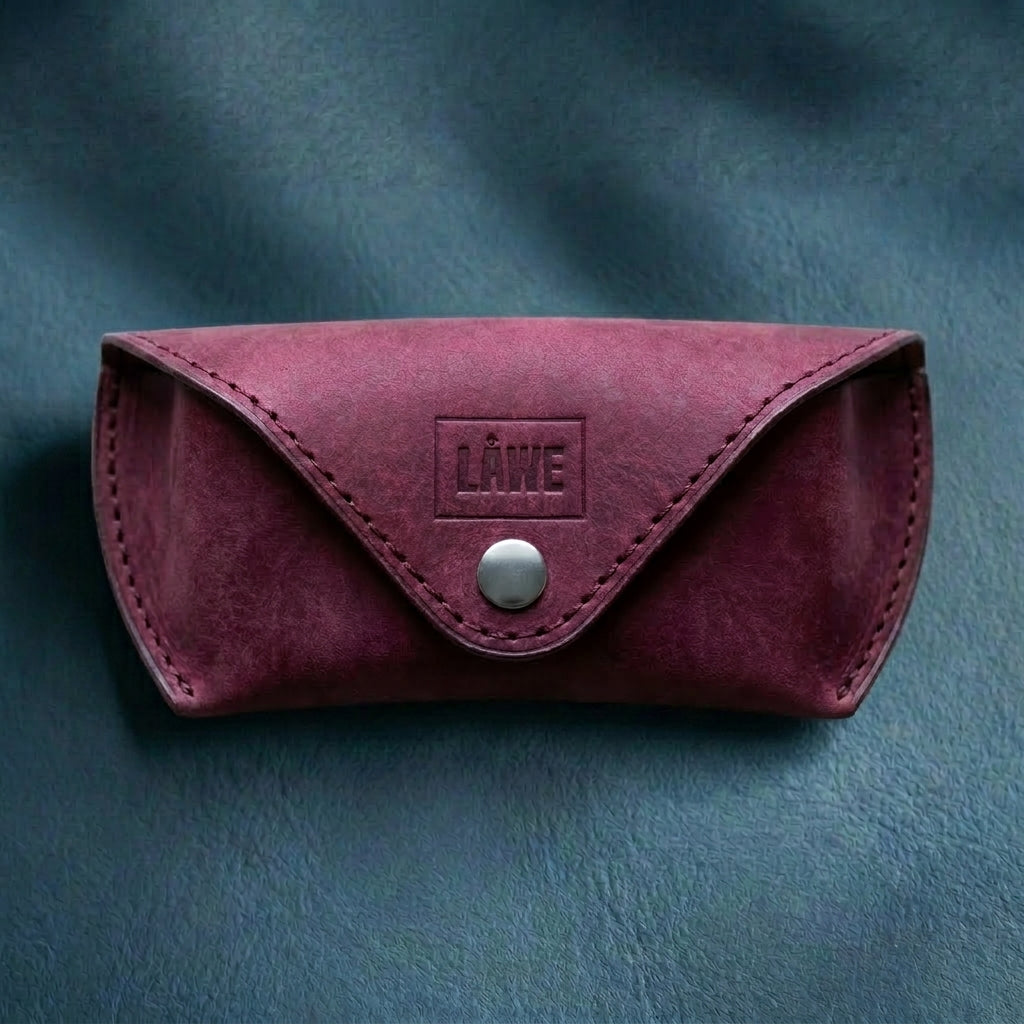 Maroon leather eyewear case with metal button closure on a grey background