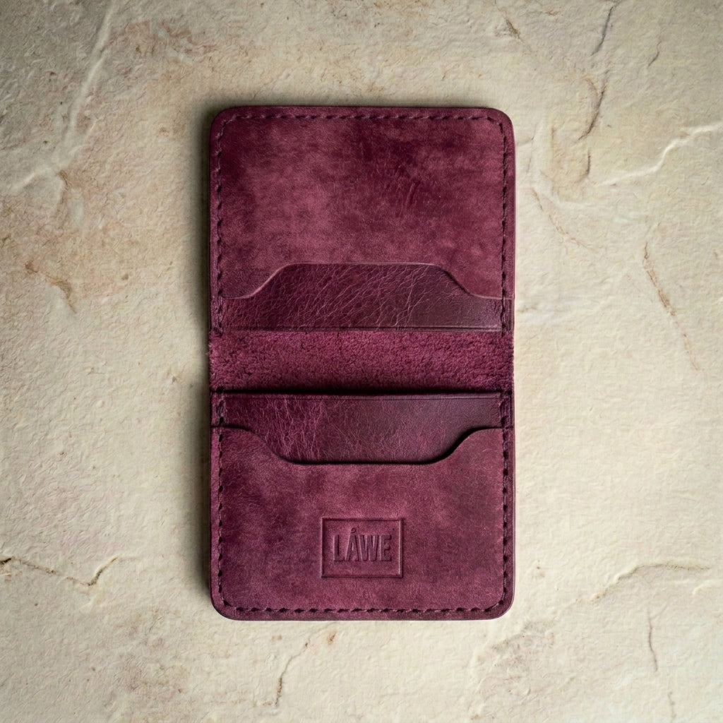 Burgundy leather wallet with 'LÅWE' branding on a beige stone surface