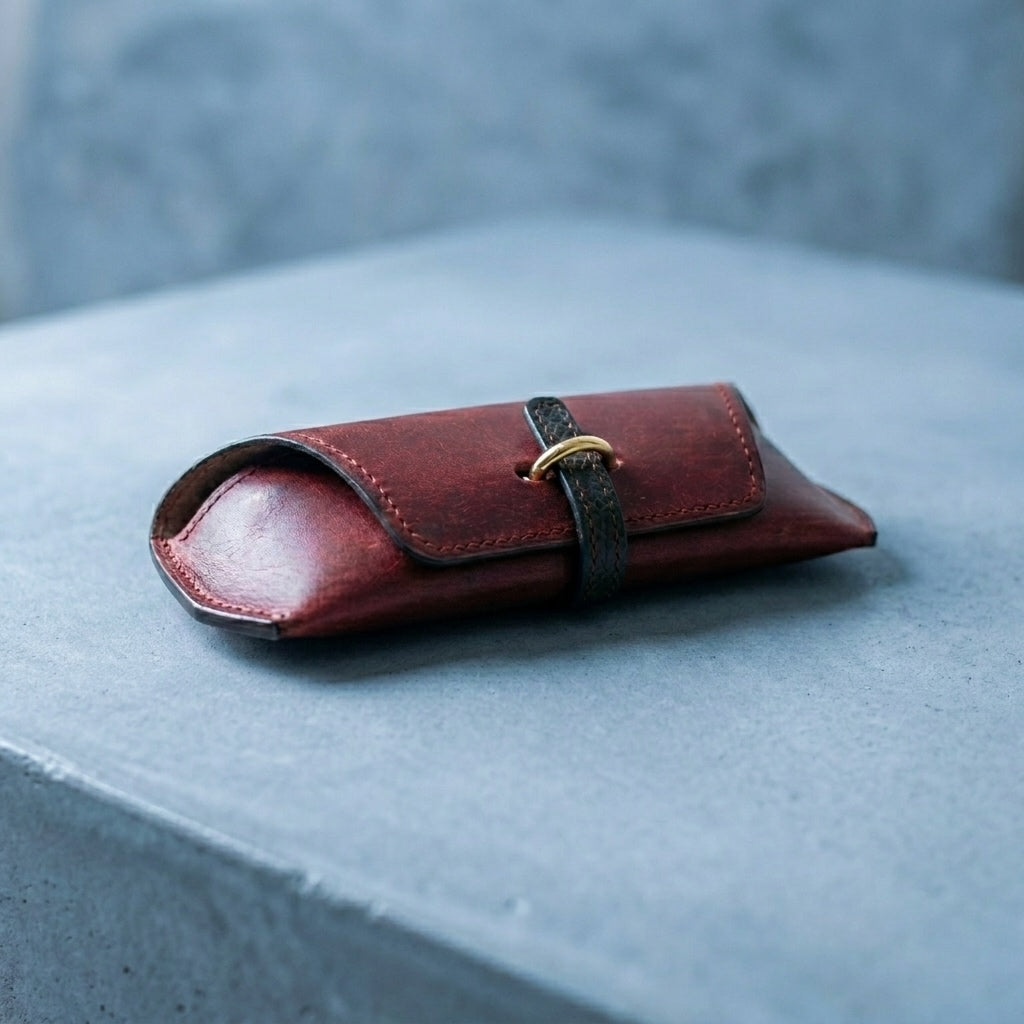 Bordeaux LÅWE Focus leather eyewear case with a strap on a grey stone surface