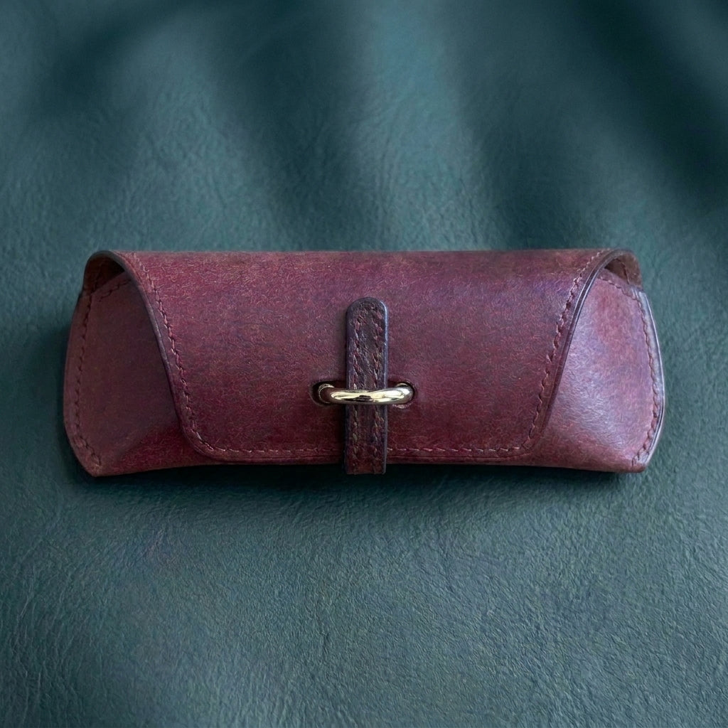Bordeaux LÅWE Focus leather eyewear case with a gold buckle on a slate textured background