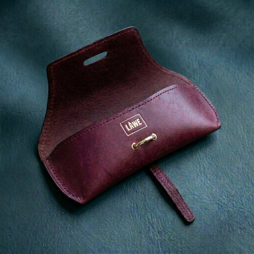 Bordeaux LÅWE Focus eyewear leather pouch with gold clasp on a teal background