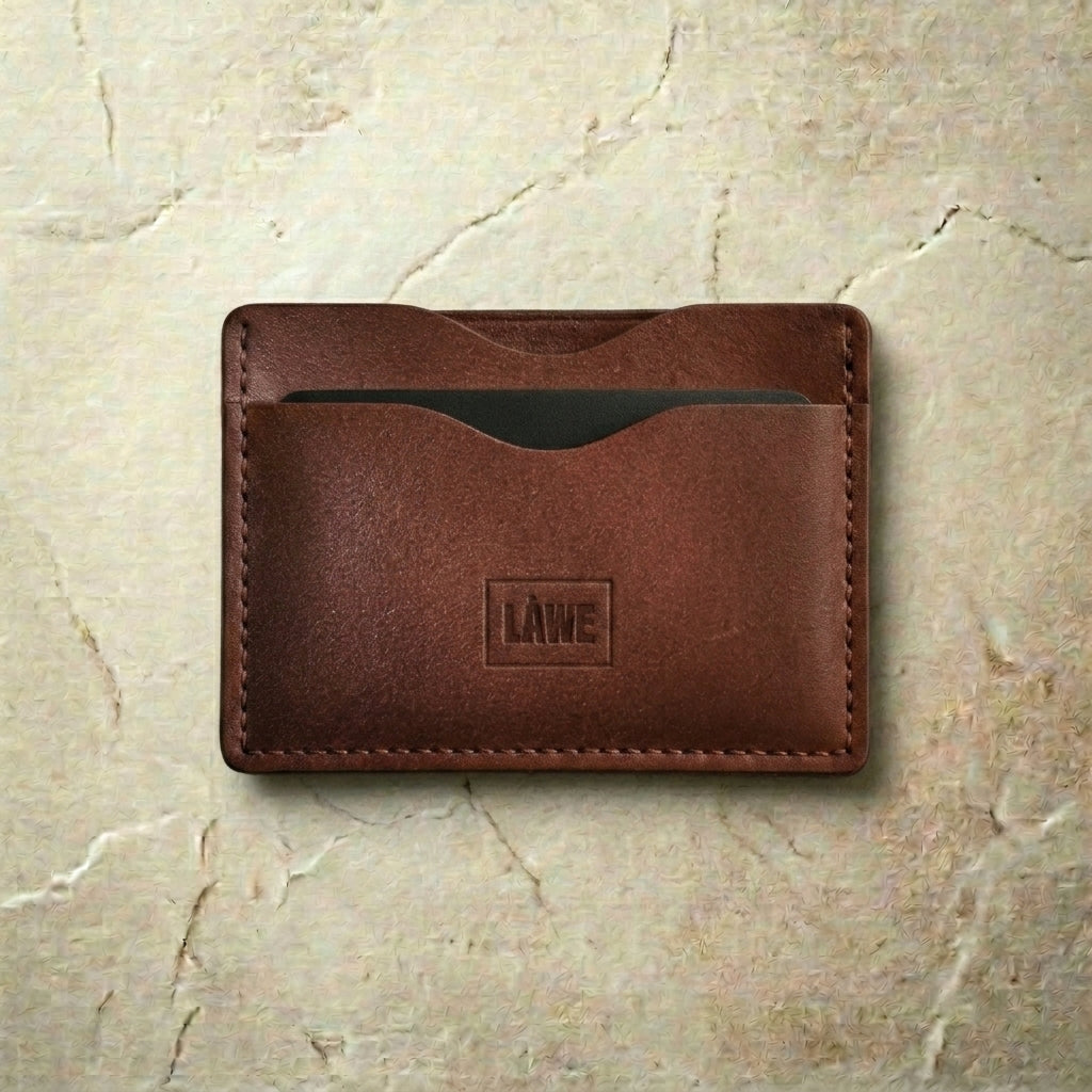 Brown leather cardholder with 'LÅWE' branding on a beige marble background