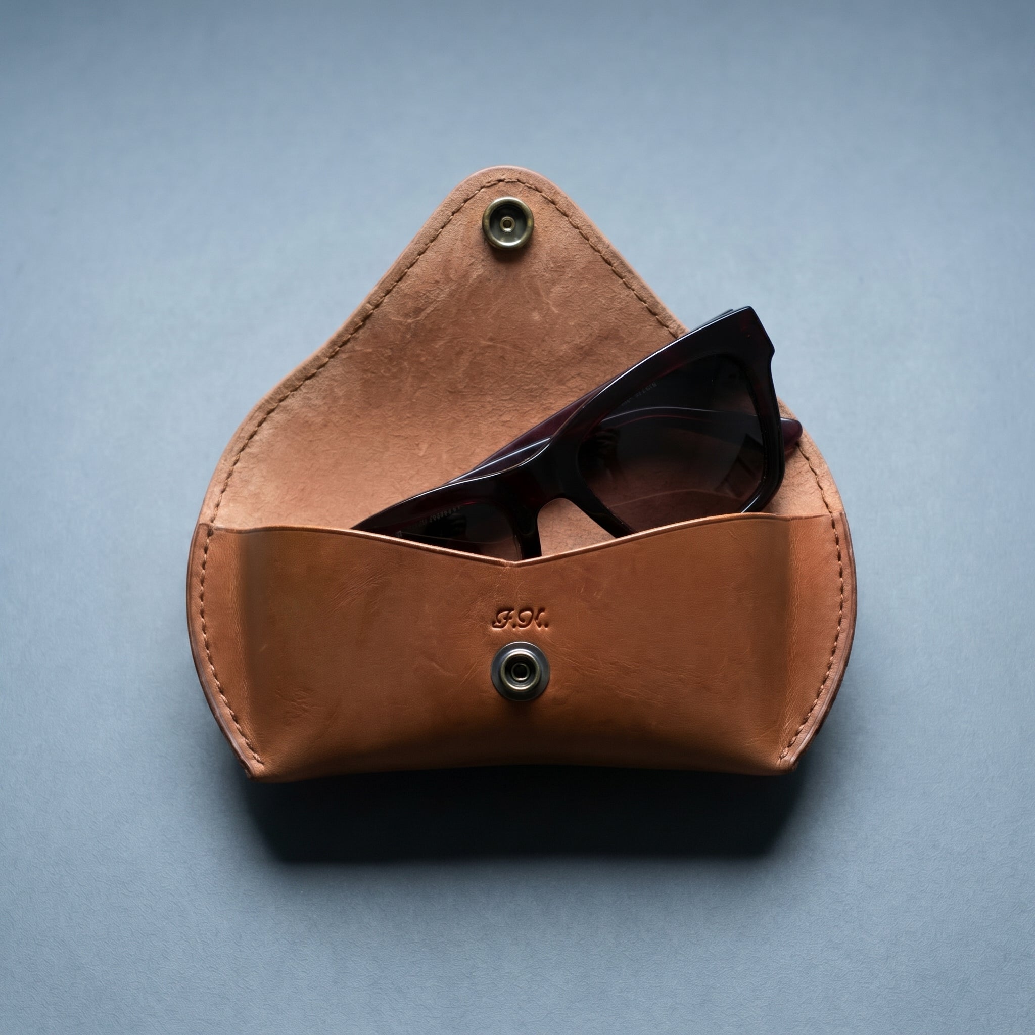 Warm brown leather sunglasses case on a gray background
