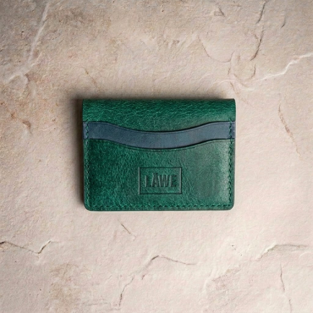 LÅWE Current fold wallet in Emerald green leather with contrasting teal accent slots closed on a textured beige stone surface