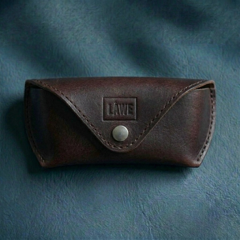 Dark brown leather eyewear case with a visible brand logo on a textured blue background
