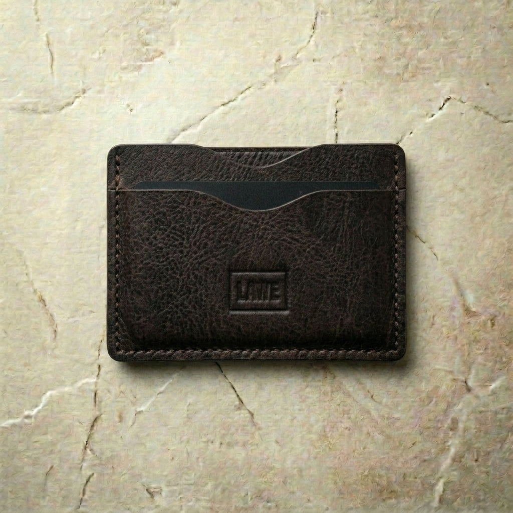 Brown leather wallet with 'LÅWE' branding on a beige marble surface
