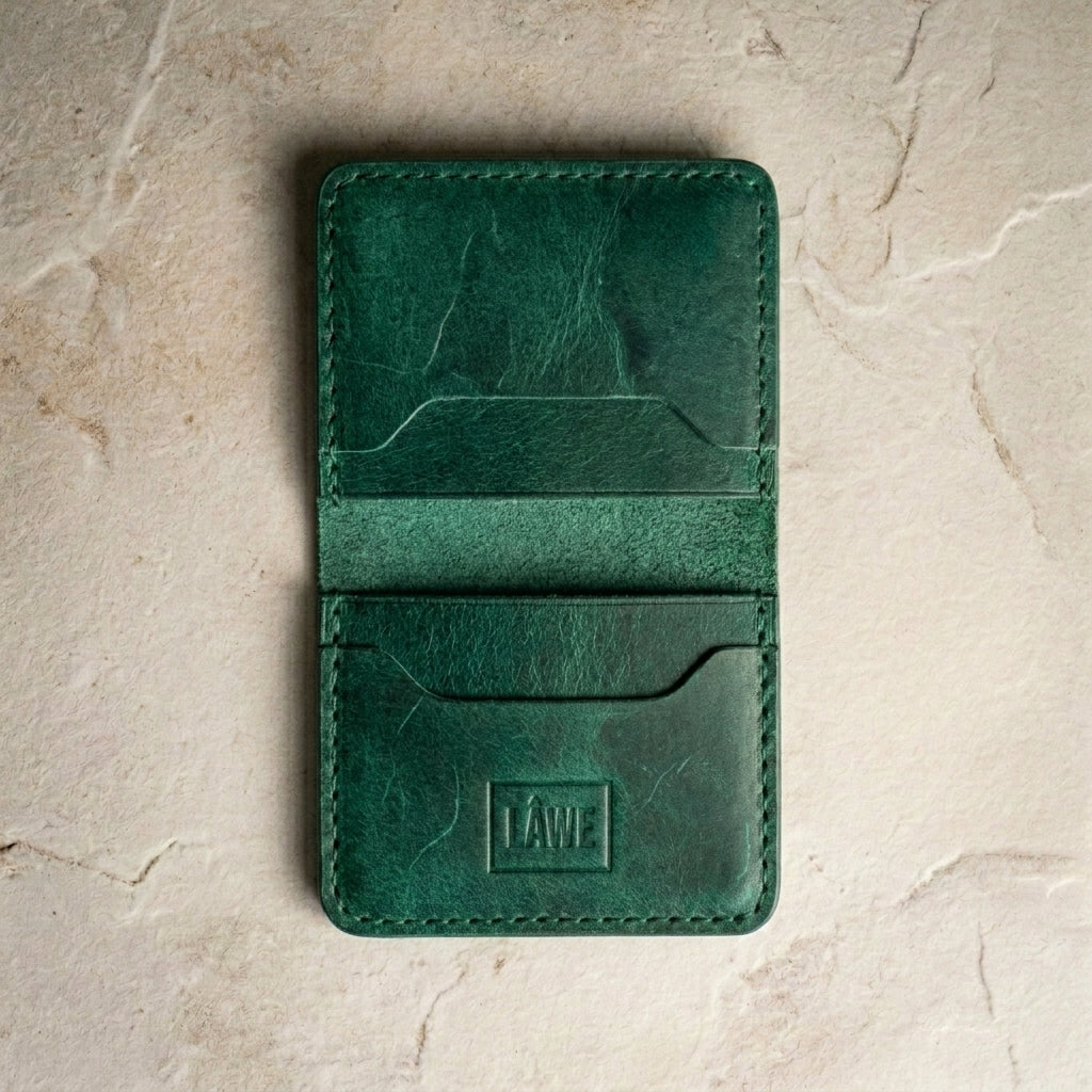 Green leather wallet with 'LÅWE' branding on a beige stone surface