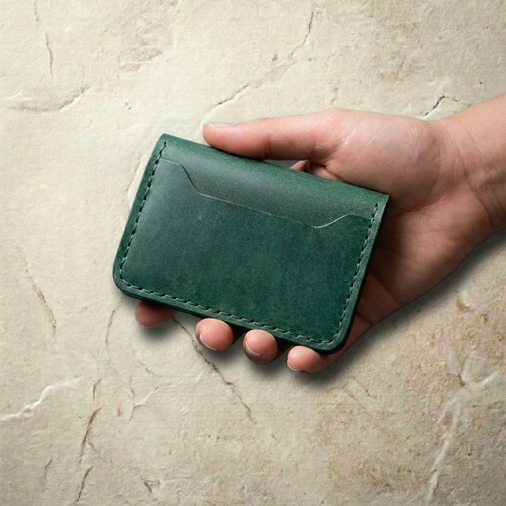 LÅWE Forest Edge - hand holding a green leather wallet on a beige marble surface