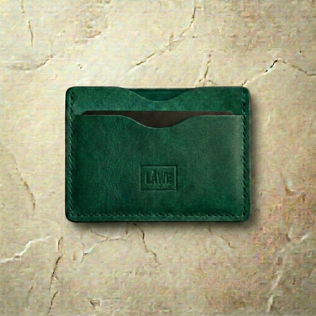 Green leather cardholder with 'LÅWE' branding on a beige marble background