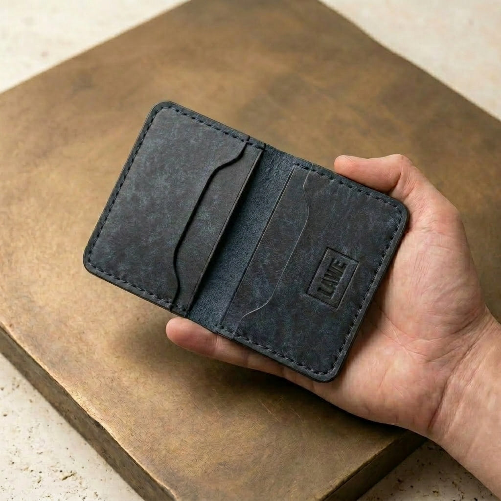Hand holding the LÅWE Slate Edge wallet on a gold surface