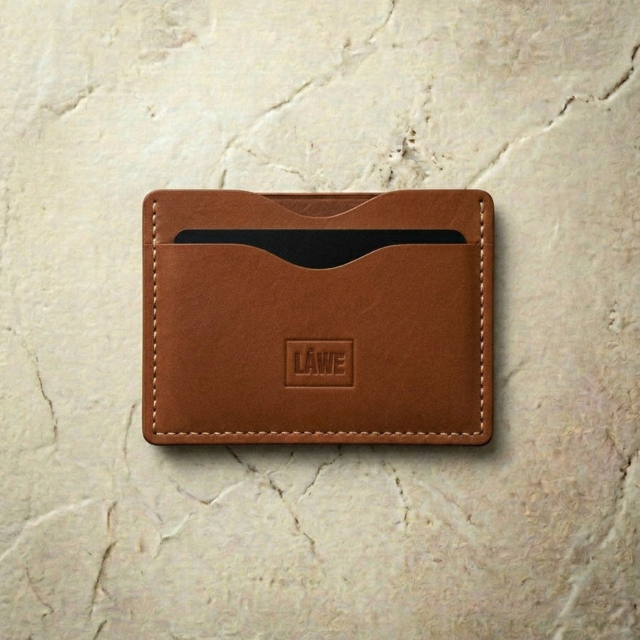 Brown leather cardholder with 'LÅWE' branding on a beige stone background