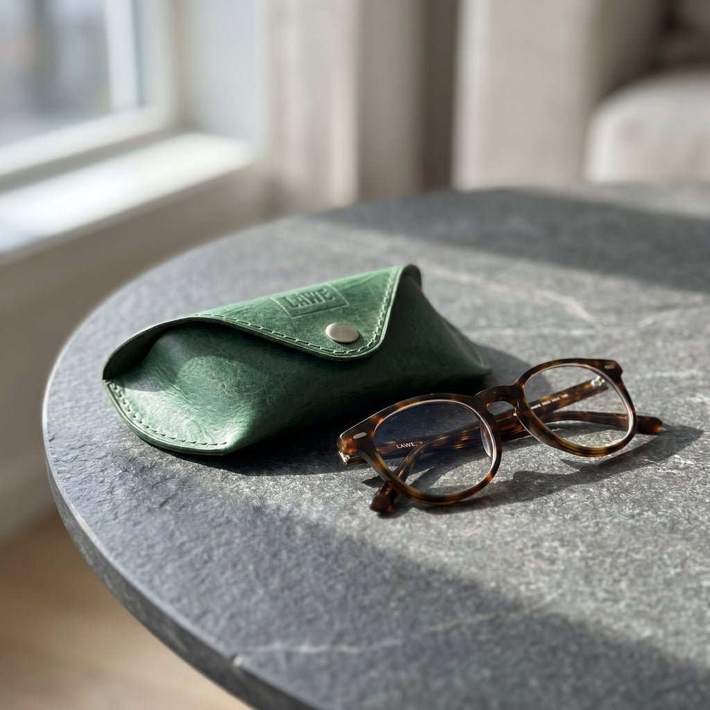 Green eyeglasses case with tortoiseshell glasses on a grey tabletop