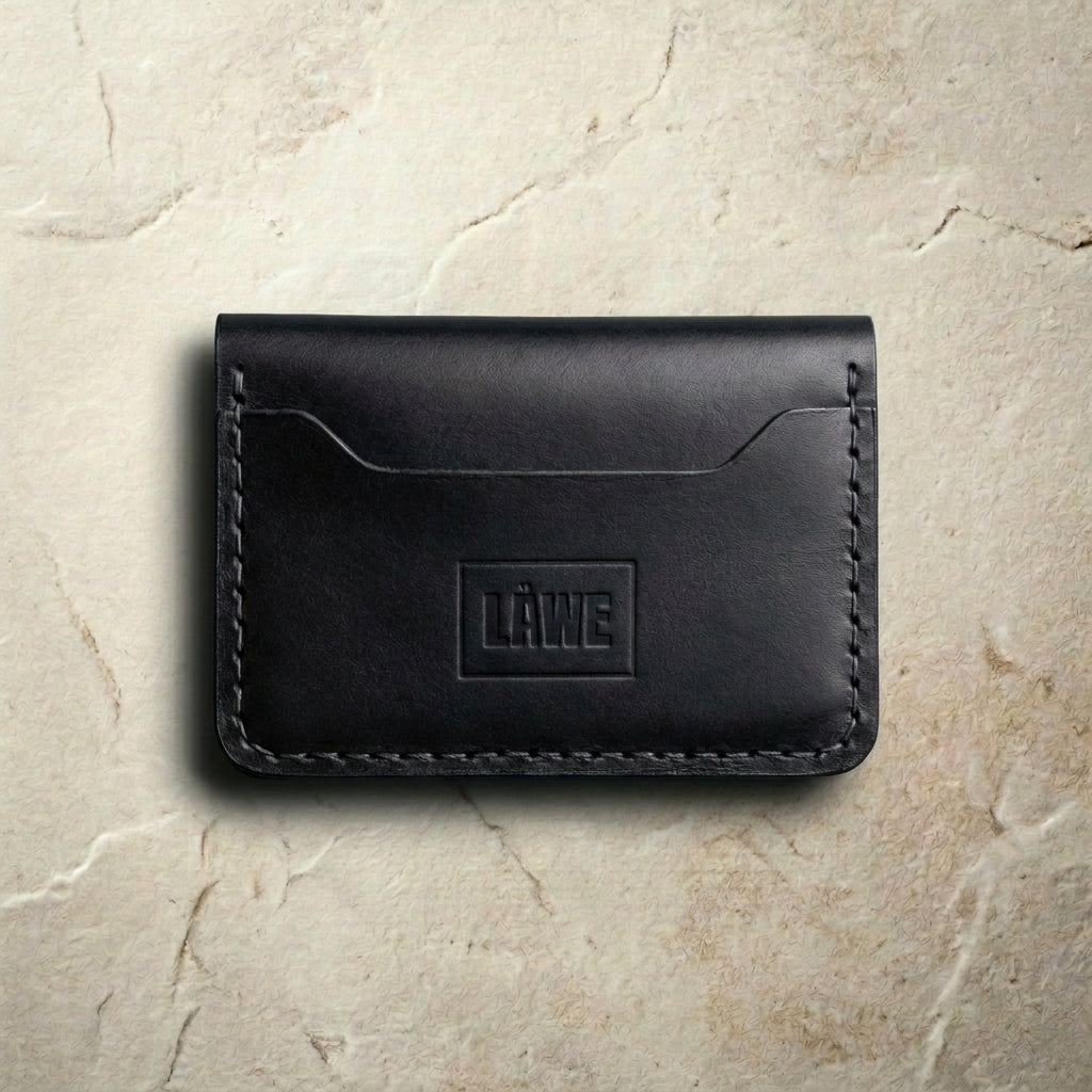 Black leather wallet with 'LÅWE' branding on a beige stone surface