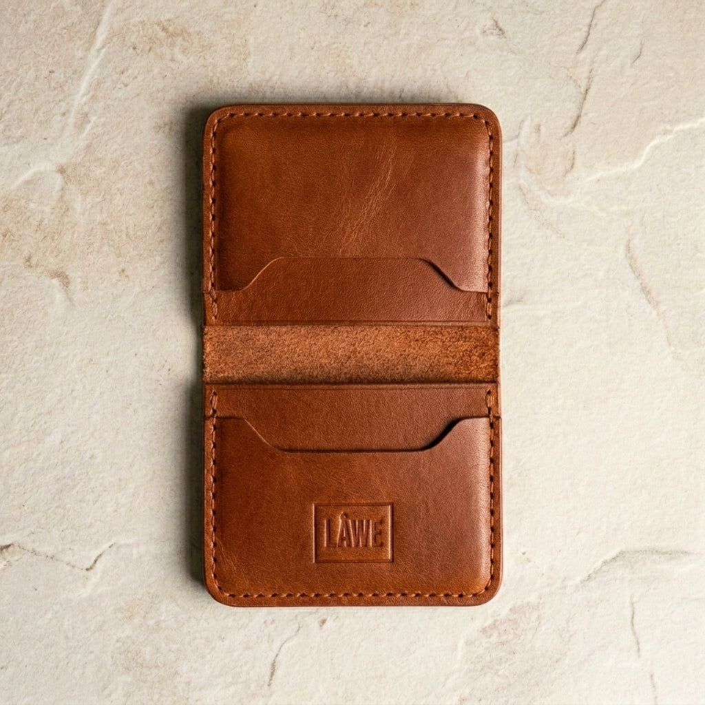 Natural brown leather wallet with 'LÅWE' branding on a beige stone surface