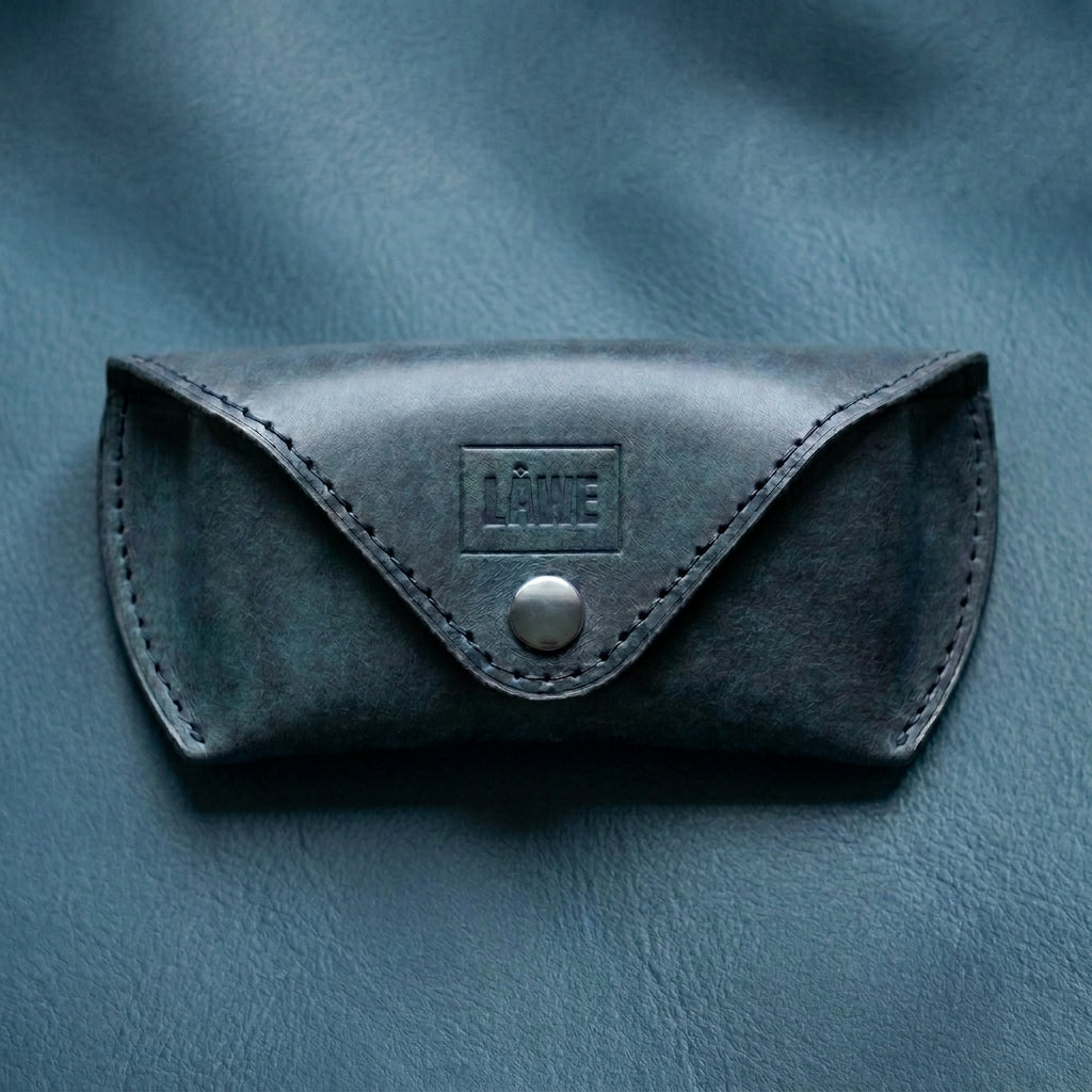 Grey leather eyewear case with a brand logo on a blue textured background