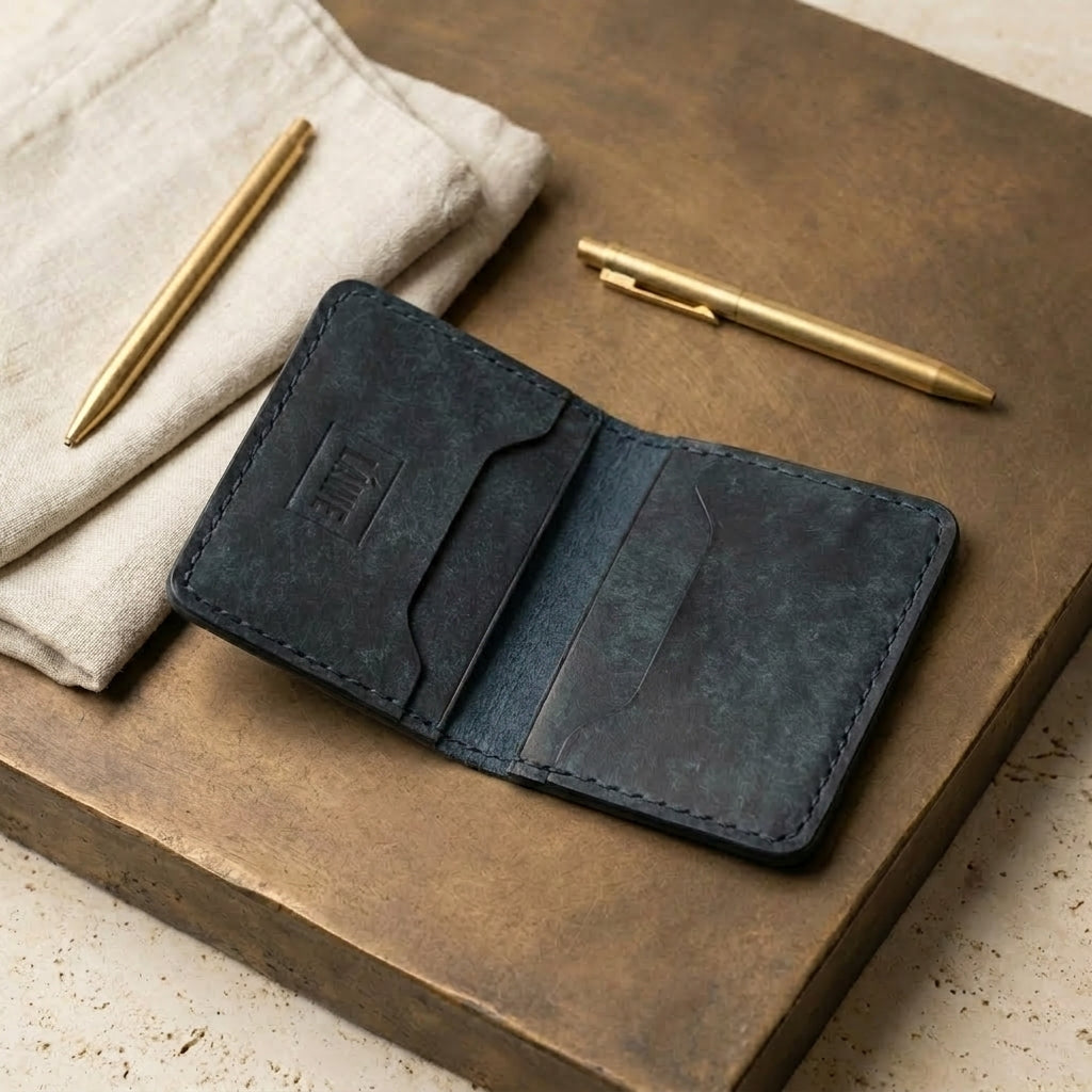 LÅWE Slate Edge leather wallet on a bronze surface with gold pens and fabric