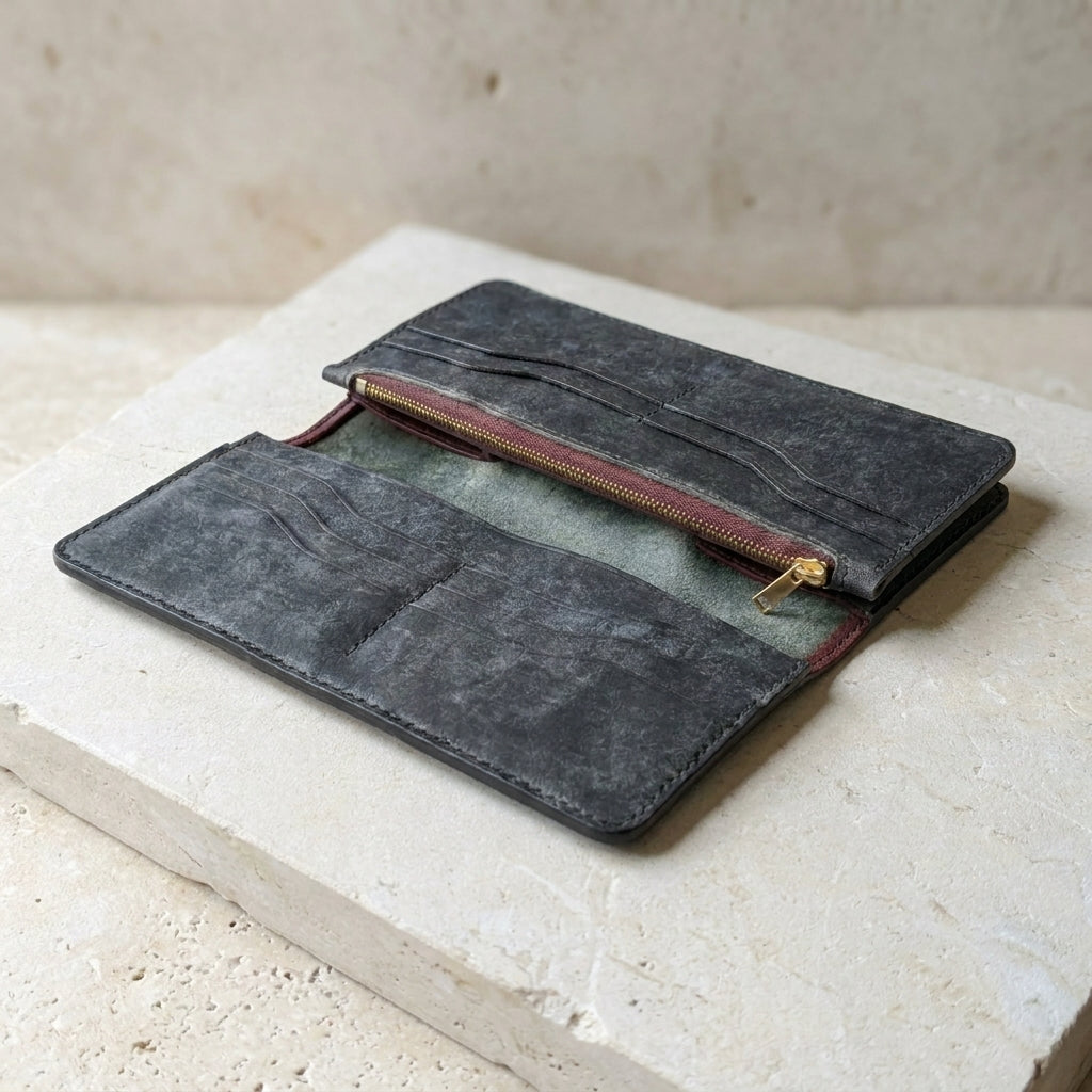 Dark gray leather pouch with a gold zipper on a light stone surface
