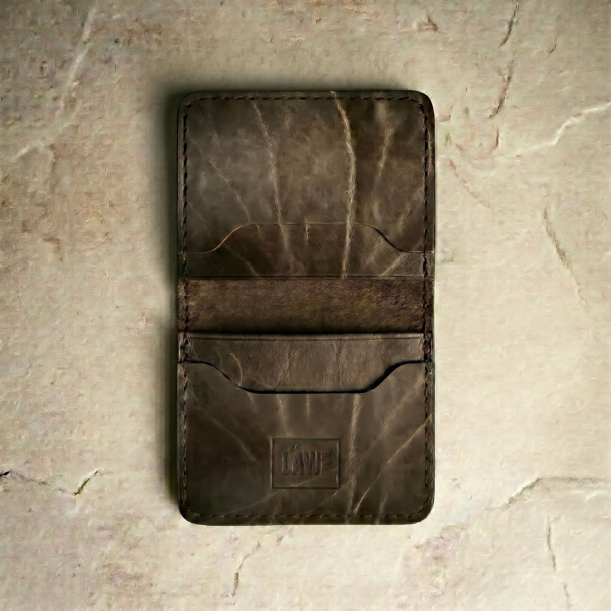 LÅWE Stone Classic Edge - olive brown leather wallet on a textured beige surface
