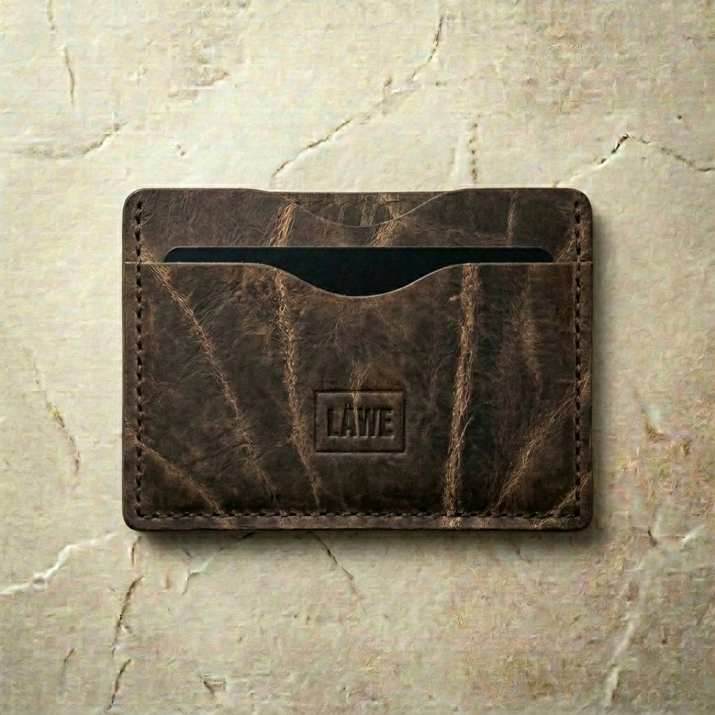 Olive grey leather cardholder with 'LÅWE' branding on a beige marble background