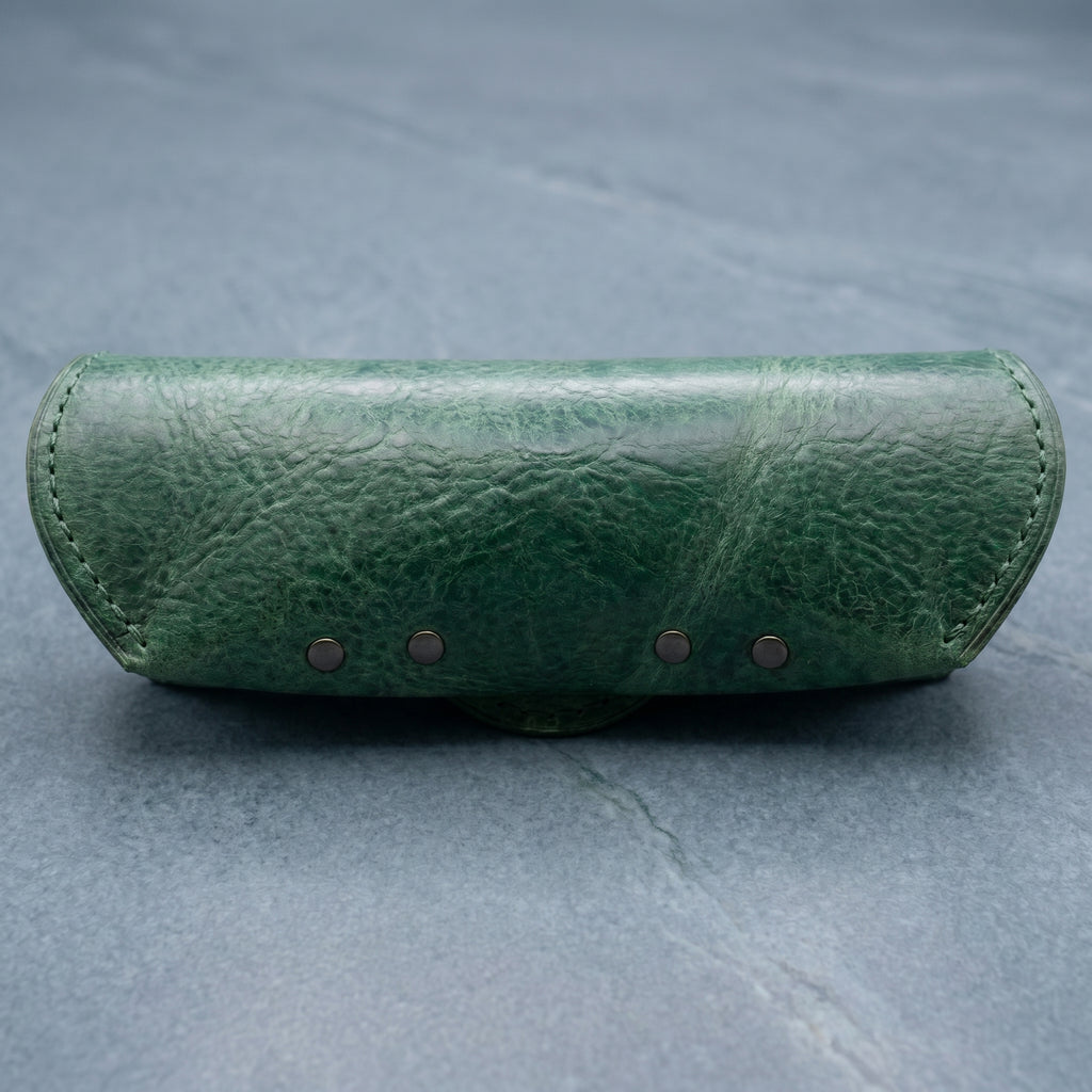 Green leather eyeglasses case with four small metal rivets on a grey background
