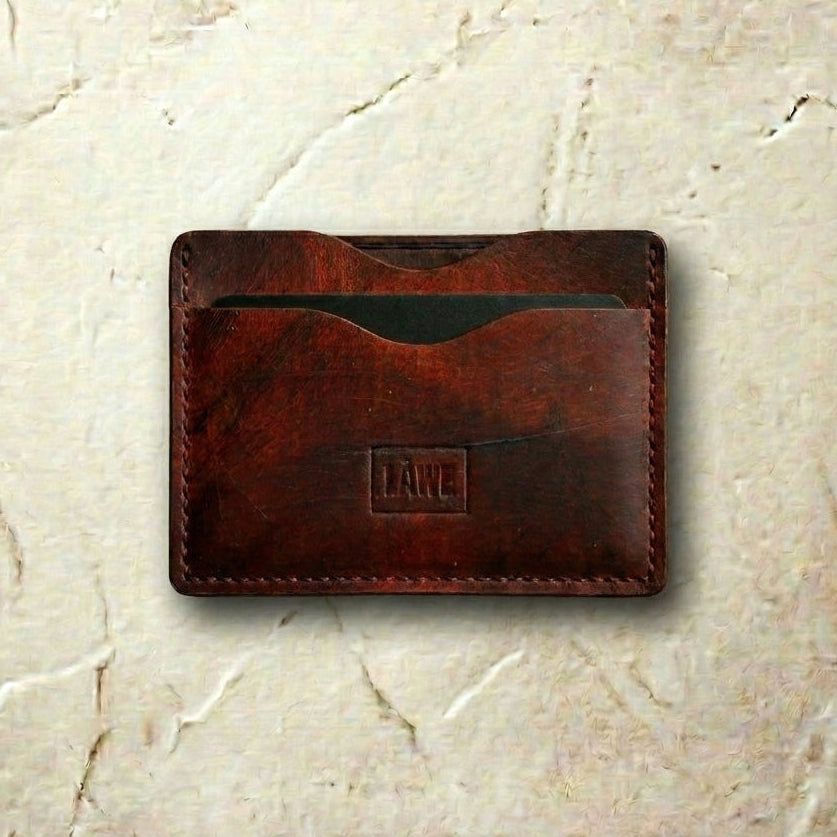 Brown  textured leather cardholder with 'LÅWE' branding on a beige marble background