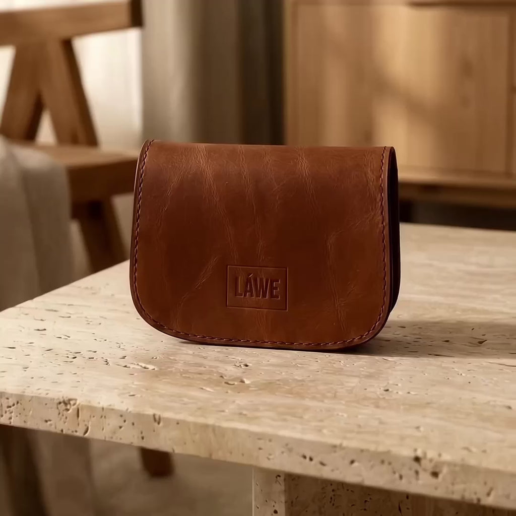 Close-up video of the LÅWE Contour brown leather wallet being opened, handled and viewed from different angles, showing its curved silhouette, layered construction, stitching and full-grain leather texture